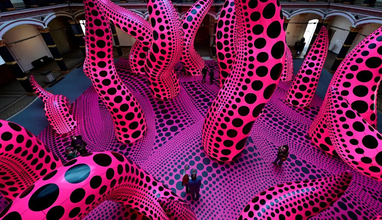 Pengunjung berjalan melewati instalasi seni berjudul 'A bouquet of love I saw in the universe' karya seniman kontemporer Jepang Yayoi Kusama dalam pameran Yayoi Kusama: A Retrospective di Atrium Martin Gropius Bau, Berlin, Jerman, Selasa (19/5/2021). (John MACDOUGALL/AFP)