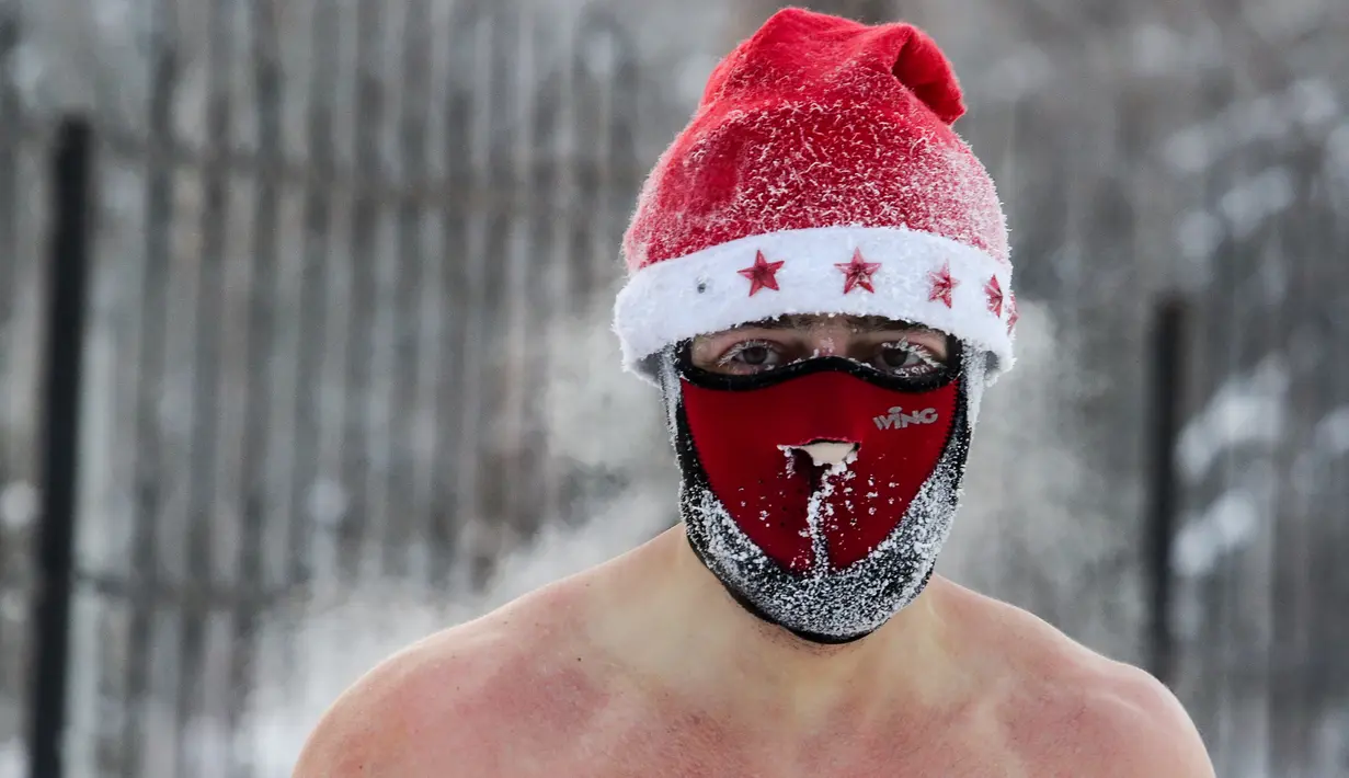 Seorang pria mengenakan masker dan topi Natal bersiap berenang di dalam air es saat suhu turun hingga minus 34 derajat celcius, di Novosibirsk, Rusia, Sabtu (26/12/2020). Konon, tradisi semacam ini mereka lakukan karena diyakini baik untuk kesehatan. (Rostislav NETISOV/AFP)