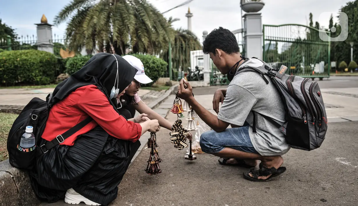 Pedagang souvenir saat menawarkan cinderamata kepada pengunjung depan gerbang masuk Monumen Nasional (Monas), Jakarta, Minggu (15/11/2020). Tutupnya Monas juga berdampak sepinya pendapatan bagi para pedagang souvenir dan jasa delman. (merdeka.com/Iqbal S Nugroho)