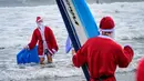 Seorang pengunjung berkostum Sinterklas berselancar dalam acara Surfing Santa yang berlangsung di Pantai Cocoa, Florida, Amerika Serikat, Selasa (24/12/2024) waktu setempat. (AFP/Giorgio Viera)