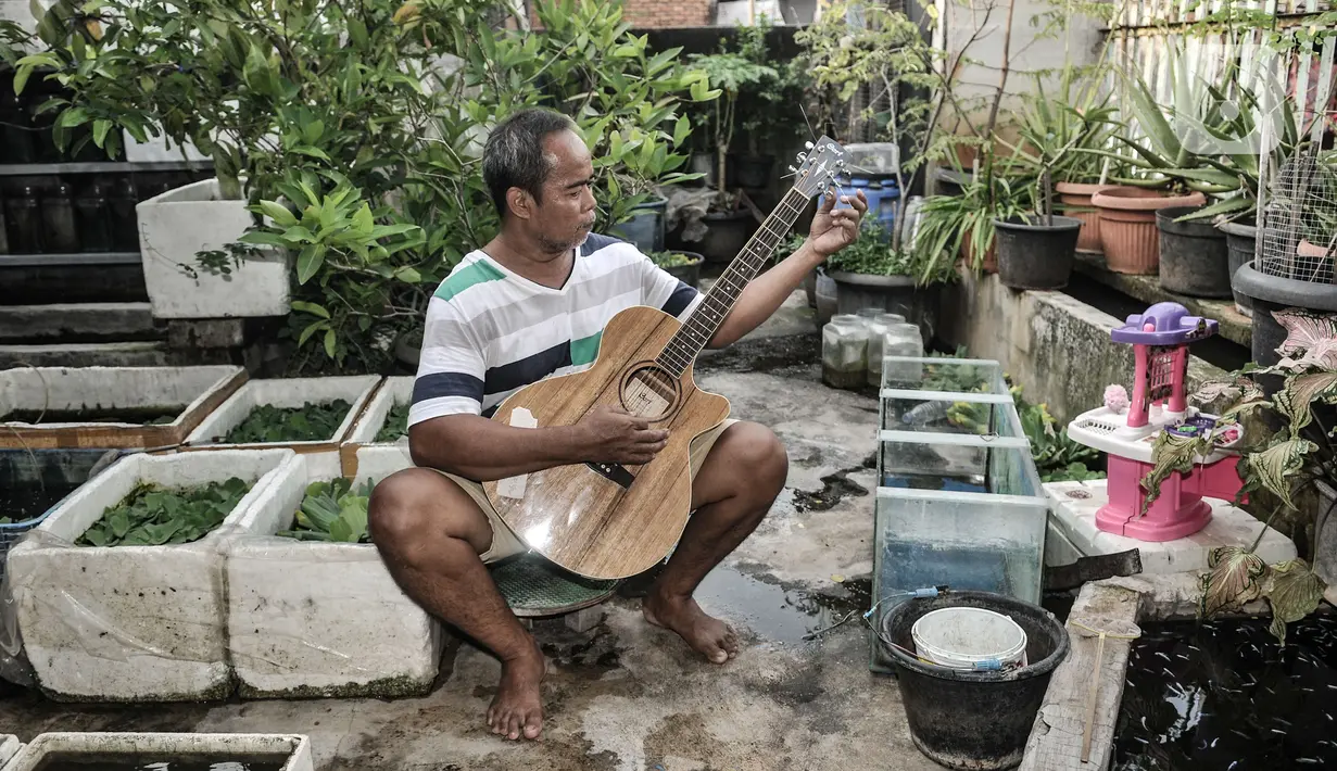 Bone bermain gitar di sela merawat ternak ikan cupang hias di workshop Bone's Costum Guitar, Jakarta, Rabu (10/3/2021). Untuk mencukupi kebutuhan sehari-hari, ayah dari 4 anak ini mencari sampingan dengan membuka ternak cupang hias sembari menunggu pelanggan gitar. (merdeka.com/Iqbal S Nugroho)