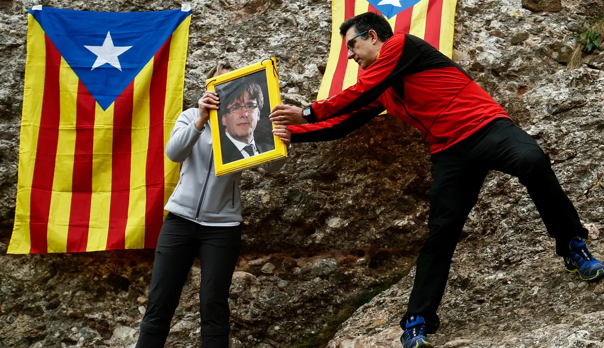 Pengunjuk rasa membawa foto presiden terguling Catalonia, Carles Puigdemont di Gunung Montserrat, Spanyol (28/4). Pegunungan Montserrat merupakan pegunungan suci yang menjadi destinasi ziarah paling terkenal bagi umat Katolik. (AFP/Pau Barrena)