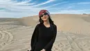 Berpose di gurun pasir, Azizah Salsha juga memilih sebuah dress panjang berwarna hitam. Ia tutupi penampilannya dengan outer yang juga berwarna hitam, sorban, dan sunglasses. [Foto: Instagram/azizahsalsha_]