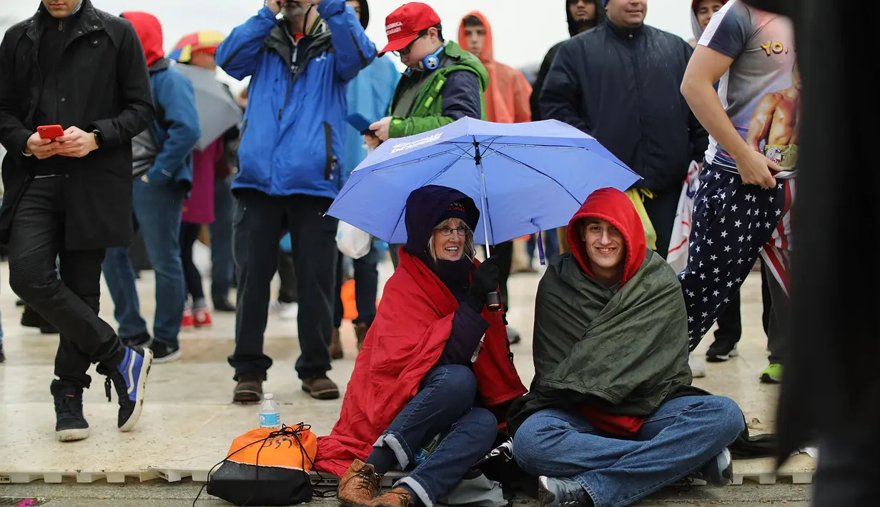 Warga berpayung saat menunggu di National Mall, Washington DC, untuk menyaksikan langsung pelantikan Trump, AS, Jumat (20/1).(AFP Photo)