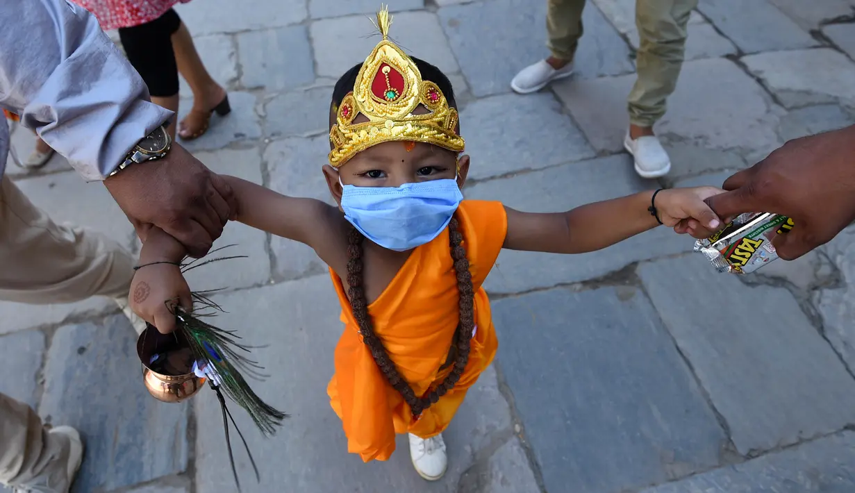 Seorang anak mengenakan kostum tradisional dan masker saat berpartisipasi dalam prosesi 'Gai Jatra', atau festival sapi, di Kathmandu, Nepal, Selasa (4/8/2020). Sapi dianggap sebagai hewan suci bagi pemeluk Hindu yang membantu jiwa-jiwa yang telah pergi mencapai surga. (PRAKASH MATHEMA/AFP)