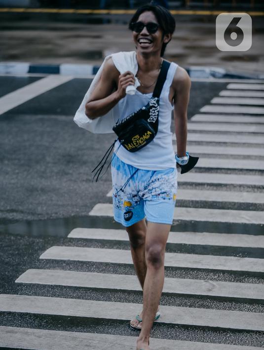 Seorang remaja mengenakan kaca mata berjalan melintasi zebra cross di Taman Sudirman, Jakarta, Rabu (6/7/2022). Tempat ini viral karena jadi ajang adu fashion anak Citayam, Bekasi hingga Bojong Gede. Mereka mengenakan kemeja flanel oversize, celana model 90-an seperti boot cut atau cutbray, sneakers klasik, dan tentu saja topi. (Liputan6.com/Faizal Fanani)