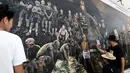 Seniman lokal menyelesaikan mural berjudul 'The Heroes' di Chiang Rai, 18 Juli 2018. Tampak lukisan wajah Saman Gunan, mantan penyelam AL Thailand yang meninggal dunia saat membantu operasi penyelamatan tim sepak bola Wild Boars. (AFP/Lillian SUWANRUMPHA)