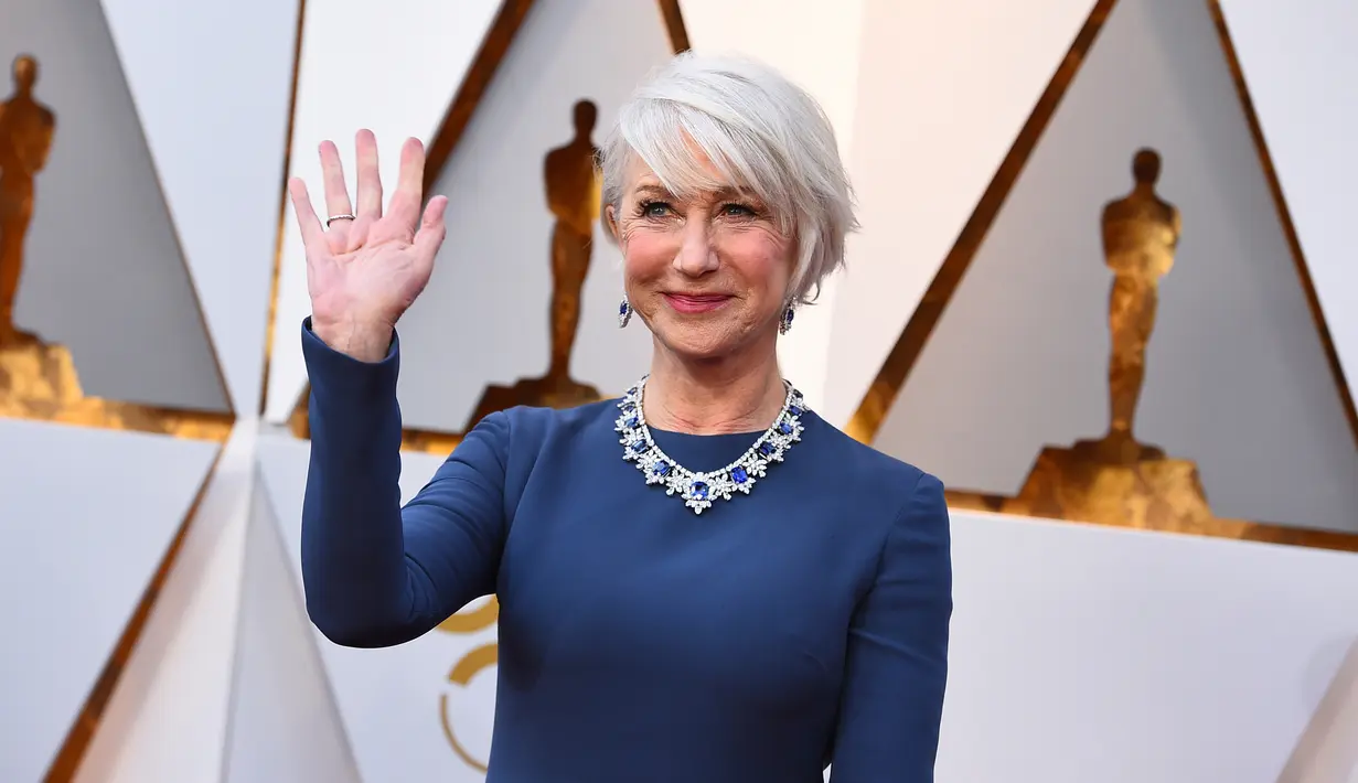 Aktris senior Helen Mirren melambaikan tangannya saat berpose di karpet merah Piala Oscar 2018 atau Academy Award ke-90, Los Angeles, Minggu (4/3). Di usia 71, Helen Mirren masih enerjik dan cantik di atas karpet. (Jordan Strauss/Invision/AP)
