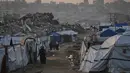 Saat ini, ratusan palet bantuan berisi peralatan medis dan kebutuhan pokok telah disiapkan di Yordania dan Mesir. Tampak dalam foto, warga Palestina berjalan melewati perkemahan tenda di tengah bangunan-bangunan yang hancur akibat serangan udara dan darat Israel di Kota Gaza, Selasa 6 Januari 2026. (AP Photo/Jehad Alshrafi)