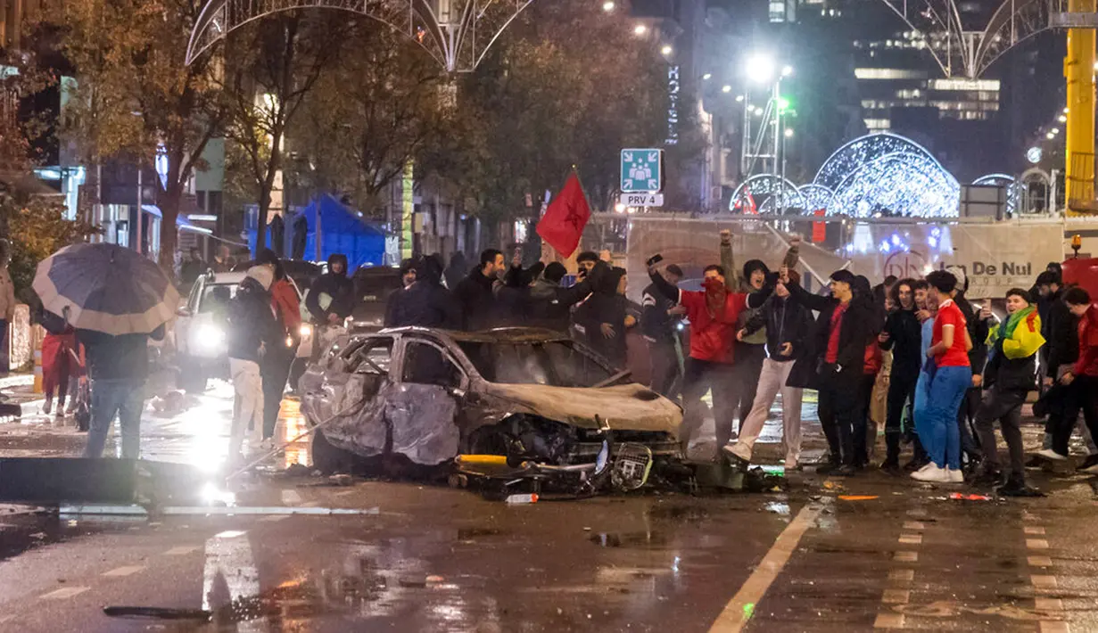 Suporter Maroko bersorak saat berdiri di samping mobil yang terbakar di Brussel, Belgia, 27 November 2022. Polisi harus menutup sebagian pusat Kota Brussel dan bergerak dengan meriam air serta gas air mata untuk membubarkan massa menyusul kerusuhan selama dan setelah Maroko menang 2-0 atas Belgia di Piala Dunia 2022. (AP Photo/Geert Vanden Wijngaert)