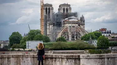 Seorang wanita mengamati Katedral Notre-Dame yang tengah dipugar di Paris, Prancis, Senin (27/4/2020). Renovasi Katedral Notre-Dame dilanjutkan kembali setelah sempat dihentikan sejak 17 Maret lalu akibat epidemi COVID-19. (Xinhua/Aurelien Morissard)