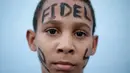Seorang anak dengan tulisan Fidel di keningnya menunggu mobil yang membawa abu Fidel Castro, lewat di Bayamo, Kuba (3/11). Sebelum dikebumikan, rakyat Kuba memberikan penghormatannya kepada Castro di Jose Marti Memorial. (Reuters/Enrique De La Osa)