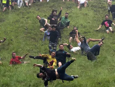 Sejumlah peserta berlari menuruni bukit curam untuk mengejar keju dalam kompetisi Cheese Rolling di Cooper's Hill di Brockworth, Gloucestershire, Inggris, Senin (28/5). Kompetisi ini diikuti ribuan peserta setiap tahunnya. (Aaron Chown/PA via AP)