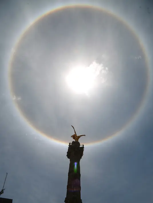 Fenomena halo matahari dengan latar depan monumen Malaikat Kemerdekaan di pusat kota Mexico City, Sabtu (7/7). Fenomena halo matahari terjadi karena pembiasan kristal es yang berada di sekitar Matahari yang membentuk semacam pelangi. (AP/Anthony Vazquez)
