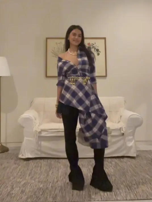 Eva Celia mengenakan dress flannel yang ia styling menjadi atasan dipadukan belt keemasan serta celana dan mini skirt hitam. [@evacelia]