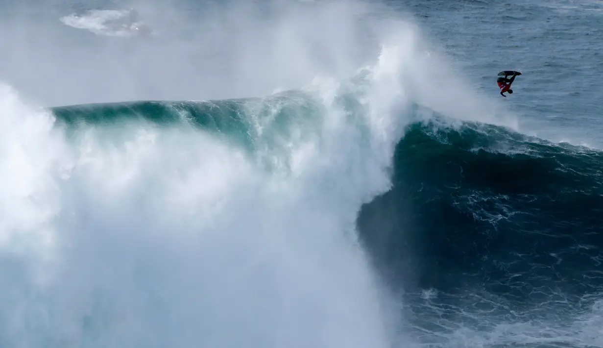 Peselancar bermanuver terbalik saat unjuk kebolehan dalam menaklukkan ombak besar di Praia do Norte atau Pantai Utara, Nazare, Portugal, Rabu (20/11/2019). Hanya peselancar profesional yang boleh bermain ombak di perairan ini. (AP Photo/Armando Franca)