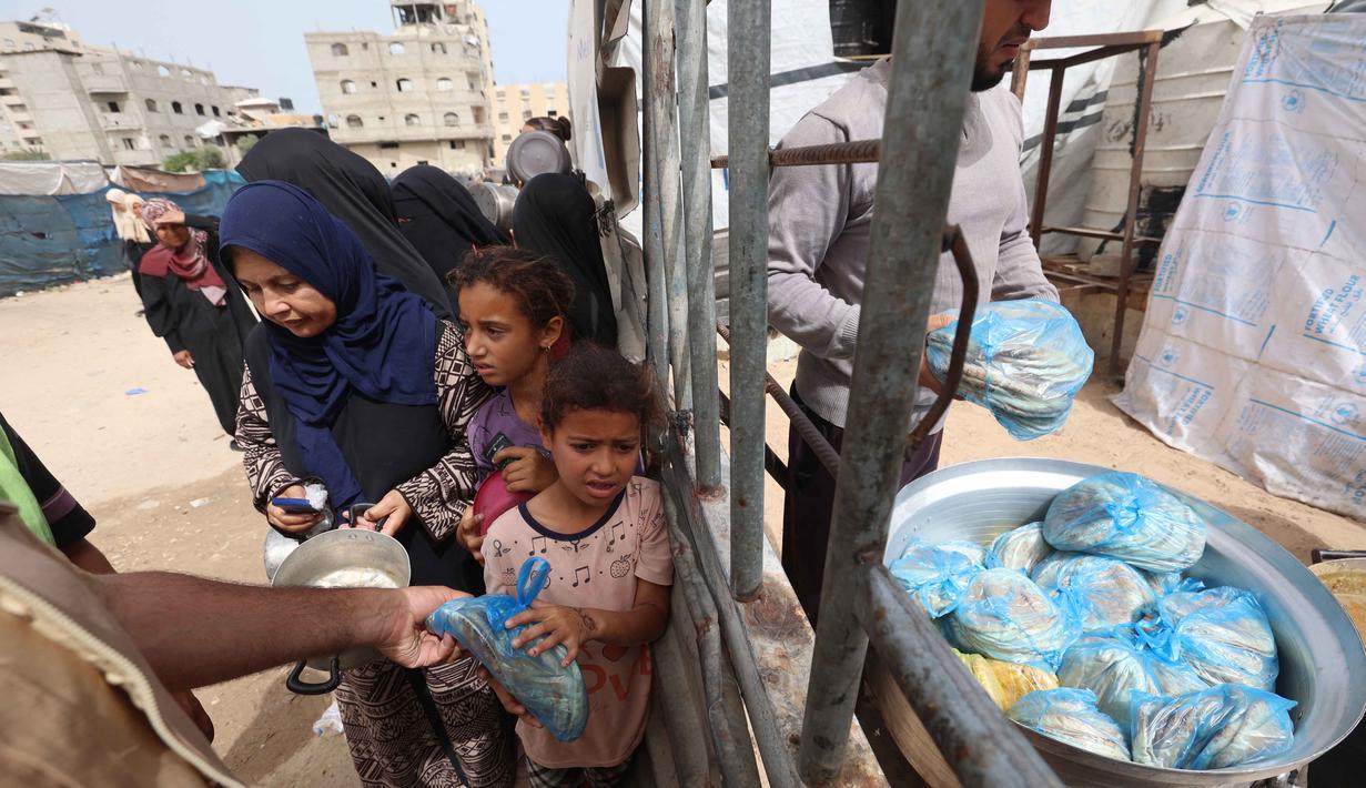 Seorang anak pengungsi Palestina mengambil sebungkus roti sementara yang lain menunggu giliran mereka dari salah satu dapur amal di kamp pengungsi Bureij, Jalur Gaza Tengah pada Senin 18 Mei 2026. (Eyad Baba/AFP)
