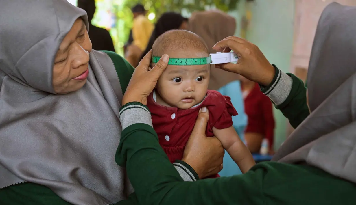 Seorang tenaga kesehatan mengukur lingkar kepala bayi selama program imunisasi massal di Surabaya pada 15 September 2025. (Juni KRISWANTO/AFP)