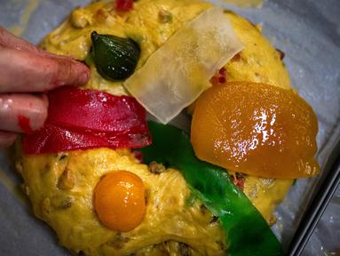 Seorang tukang roti meletakkan buah-buahan mengkristal di atas Bolo Rei atau Kue Raja yang siap untuk dioven di toko roti Padaria da Ne, Amadora, Portugal, 16 Desember 2022. Kue berbentuk cincin ini adalah salah satu sajian khas Natal di Portugal. (CARLOS COSTA/AFP)