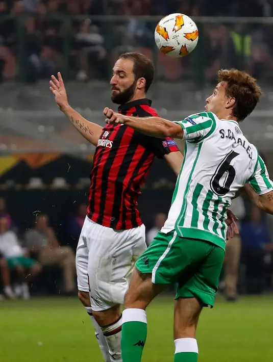 Pemain AC Milan, Gonzalo Higuain (kiri) berebut bola dengan pemain Real Betis Sergio Canales saat bertanding dalam Grup F Liga Europa di Stadion San Siro, Milan, Italia, Kamis (25/10). AC Milan kalah 1-2. (AP Photo/Antonio Calanni)