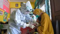Perawat mengenakan alat pelindung diri saat menyuntikkan vaksin campak kepada seorang anak di Hari Perawat Internasional di Palu, Indonesia, Selasa (12/5/2020). Hari Perawat Internasional diperingati setiap tanggal 12 Mei yang bertepatan dengan kelahiran Florence Nightingale. (MUHAMMAD RIFKI/AFP)
