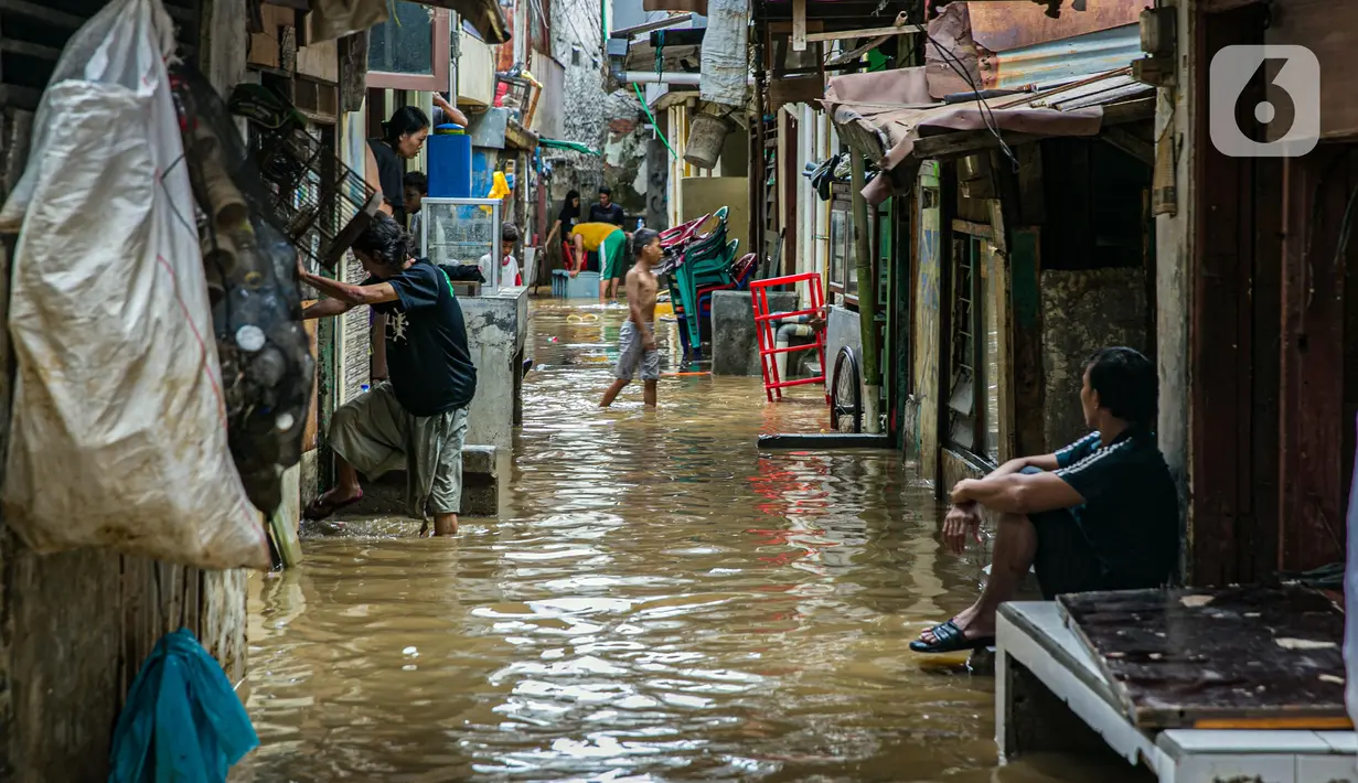Seorang pria duduk di depan rumah saat warga lainnya membersihkan barang-barang yang terendam banjir di permukiman kawasan Kampung Melayu, Jakarta, Selasa (9/2/2021). Banjir yang berangsur surut dimanfaatkan warga untuk membersihkan rumah dan barang-barang. (Liputan6.com/Faizal Fanani)