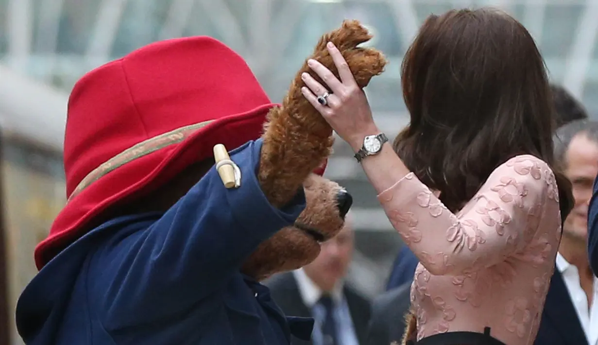 Kate Middleton berdansa dengan seorang aktor yang mengenakan kostum Paddington di stasiun kereta Paddington, London, Senin (16/10). Kate berdansa dalam iringan band yang memainkan lagu soundtrack untuk film kedua Paddington. (Jonathan Brady/Pool via AP)