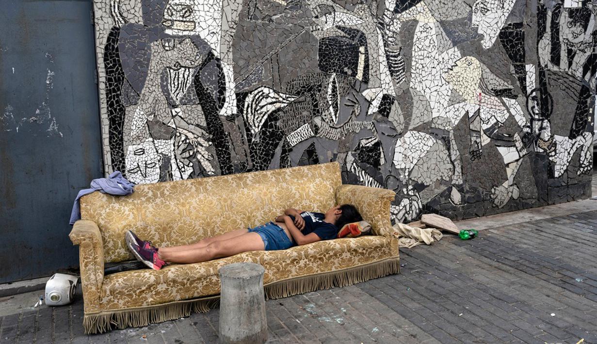 Seorang wanita tidur di sofa yang dibuang di trotoar samping mural lukisan "Guernica" karya Pablo Picasso di lingkungan Padre Carlos Mugica, Buenos Aires, Argentina, Kamis (14/12/2023). Pemerintah Argentina memotong subsidi transportasi dan energi serta mendevaluasi peso sebesar 50 persen sebagai bagian dari tindakan mengejutkan yang menurut Presiden Javier Milei diperlukan untuk menghadapi keadaan darurat ekonomi. (AP Photo/Rodrigo Abd)
