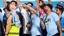 Pemain Manchester City, Jack Grealish (kiri), menggunakan rompi proyek disaat pemain lainnya memakai seragam dalam perayaan Trebele Winners di kota Manchester, Selasa (13/6/2023) dini hari WIB. Salah satu rekan satu timnya, Kalvin Phillips (tengah) bahkan menyuguhkan minuman beralkhol langsung ke mulut Grealish. (AFP/Oli Scarff)