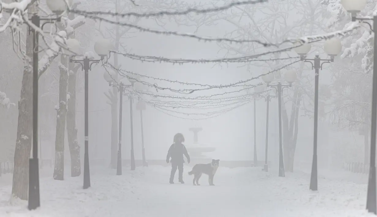 Seorang pria berjalan-jalan dengan anjingnya di taman saat suhu turun hingga sekitar -50 derajat (-58 derajat Fahrenheit) di Yakutsk, Rusia pada Rusia, Sabtu (16/1/2021).  Yakutsk atau Yakutia tersohor sebagai kota terdingin di dunia. (AP Photo/Tatiana Gasich)