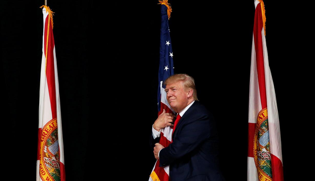 Capres AS dari Partai Republik, Donald Trump memeluk bendera AS saat melakukan kampanye menyapa pendukungnya di Tampa, Florida, AS (24/10). (REUTERS/Jonathan Ernst)