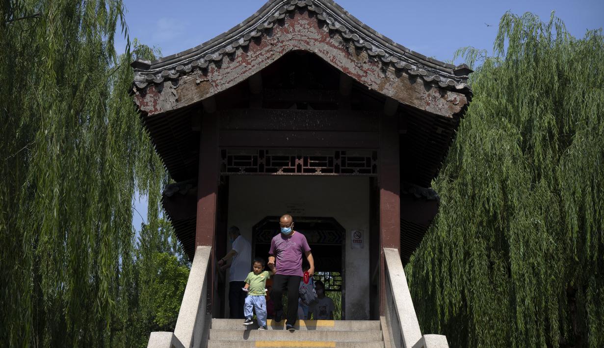 Seorang pria bermasker membantu seorang anak laki-laki menyeberangi jembatan di sebuah taman umum di Beijing, Jumat (8/7/2022). Keputusan mandat vaksin Covid-19 bagi penduduk Beijing menimbulkan pro dan kontra di kalangan penduduk. Banyak dari mereka beranggapan, kebijakan itu akan sangat berdampak pada kehidupan sehari-hari. (AP Photo/Mark Schiefelbein)