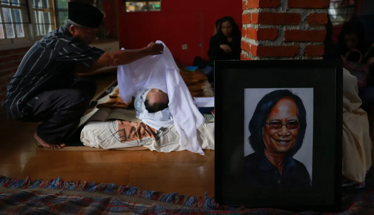 Salah seorang membuka kain putih penutup kepala lelaki yang memiliki nama asli Koesyono Koeswoyo itu. Suasana duka menyelimuti kediamannya di kawasan Tangerang Selatan. (Adrian Putra/Bintang.com)