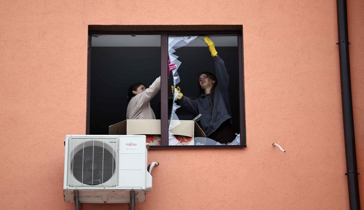 Layanan Darurat Ukraina melaporkan, delapan orang, termasuk seorang anak, berhasil diselamatkan dari reruntuhan bangunan yang hancur. Tampak dalam foto, warga setempat membersihkan pecahan kaca dari jendela yang pecah di sebuah bangunan tempat tinggal setelah serangan udara di Sofiivska Borshchagivka, wilayah Kyiv pada Minggu 22 Februari 2026. (Henry NICHOLLS/AFP)