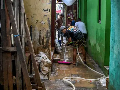 Warga membersihkan jalan di depan rumah mereka yang dipenuhi lumpur setelah banjir melanda lingkungan mereka setelah hujan deras di Jakarta pada Senin 7 Juli 2025. (BAY ISMOYO/AFP)
