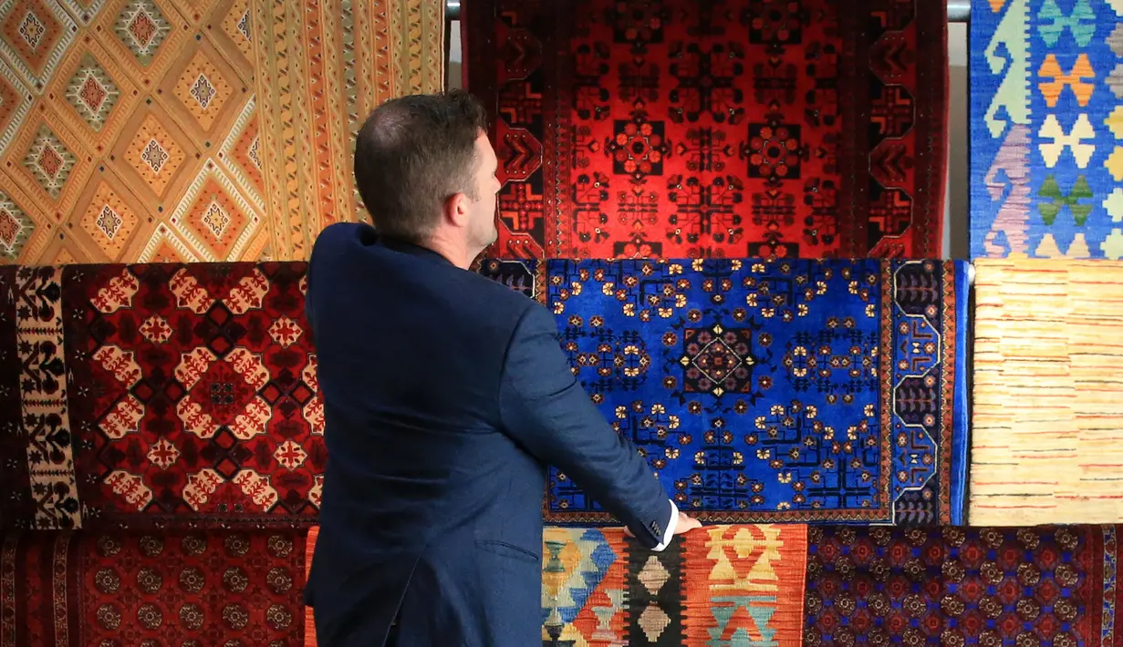 Pemilik The Afghan Rug Shop James Wilthew mengatur pajangan di tokonya di Hebden Bridge, Inggris, 20 Agustus 2021. Bisnis yang menjual karpet tenunan tangan warna-warni dan kaca buatan tangan dari Afghanistan ini takut akan pemasok mereka setelah Taliban menguasai Afghanistan. (LINDSEY PARNABY/AFP)