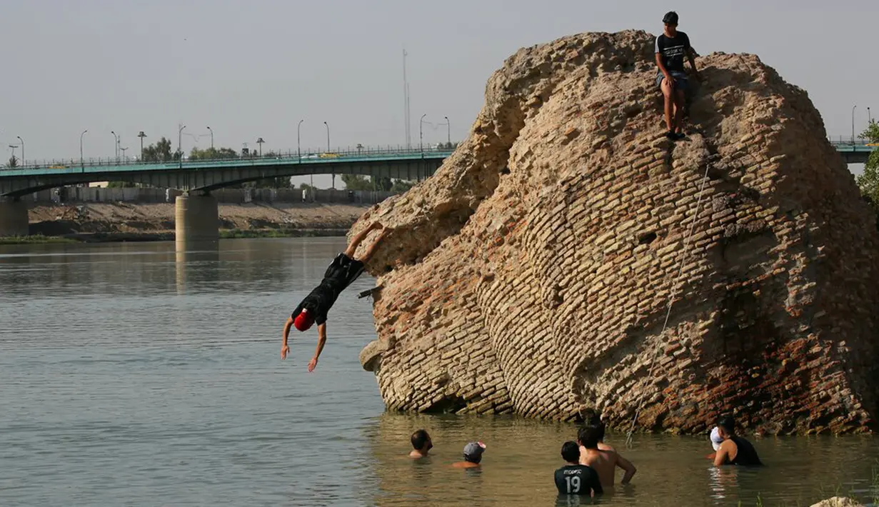 Anak-anak terjun dari reruntuhan bangunan tua ke Sungai Tigris untuk mendinginkan diri dari cuaca panas di Baghdad, Irak, Kamis (1/7/2021). Pemerintah Irak menetapkan 1 Juli 2021 sebagai hari libur resmi di Baghdad karena gelombang panas yang menyengat. (AP Photo/Khalid Mohammed)