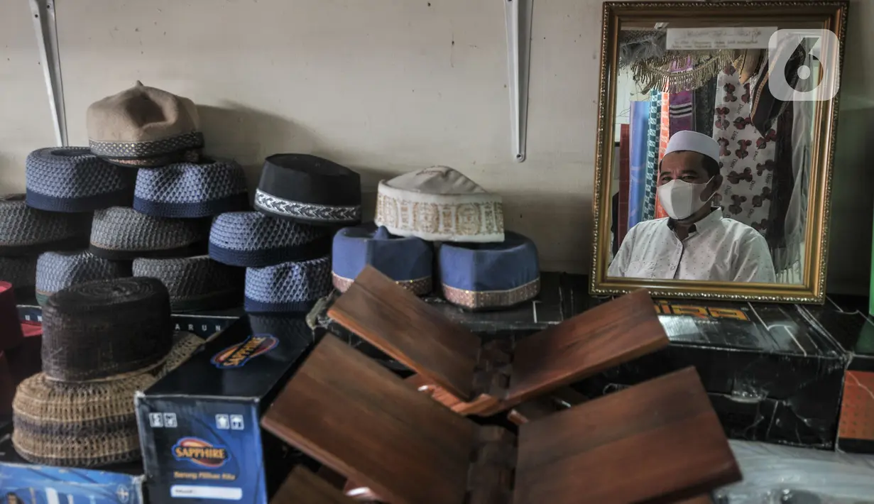 Wajah Edi terlihat di refleksi cermin saat berjaga di toko oleh-oleh haji miliknya di Jalan Raya Pondok Gede, Jakarta, Rabu (21/7/2021). (merdeka.com/Iqbal S. Nugroho)