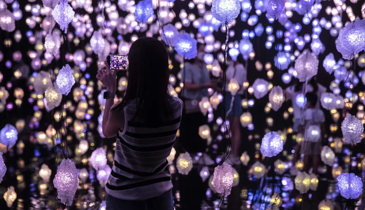 Seorang wanita mengambil foto "Pixel Forest" oleh seniman Swiss Pipilotti Rist, instalasi seni dari 3000 lampu LED pahatan tangan yang digantung di langit-langit di Tai Kwun di Hong Kong (18/8/2022). (AFP/Isaac Lawrence)