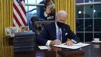 Presiden Joe Biden menandatangani perintah eksekutif pertamanya di Ruang Oval, Gedung Putih di Washington, Rabu (20/1/2021). Pada hari pertamanya menjabat, Presiden Amerika Serikat Joe Biden menandatangani sejumlah tindakan eksekutif di Gedung Putih. (AP Photo/Evan Vucci)