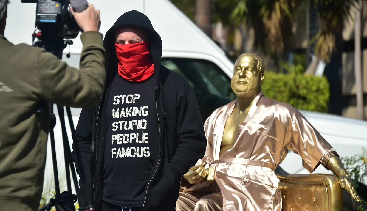 Seniman Plastic Jesus berpose dekat patung produser film, Harvey Weinstein yang dipajang dekat lokasi ajang Piala Oscar atau Academy Awards ke 90 di Hollywood, Kamis (1/3). Patung tersebut berwajah dan berukuran seperti Weinstein. (Frederic J. BROWN/AFP)