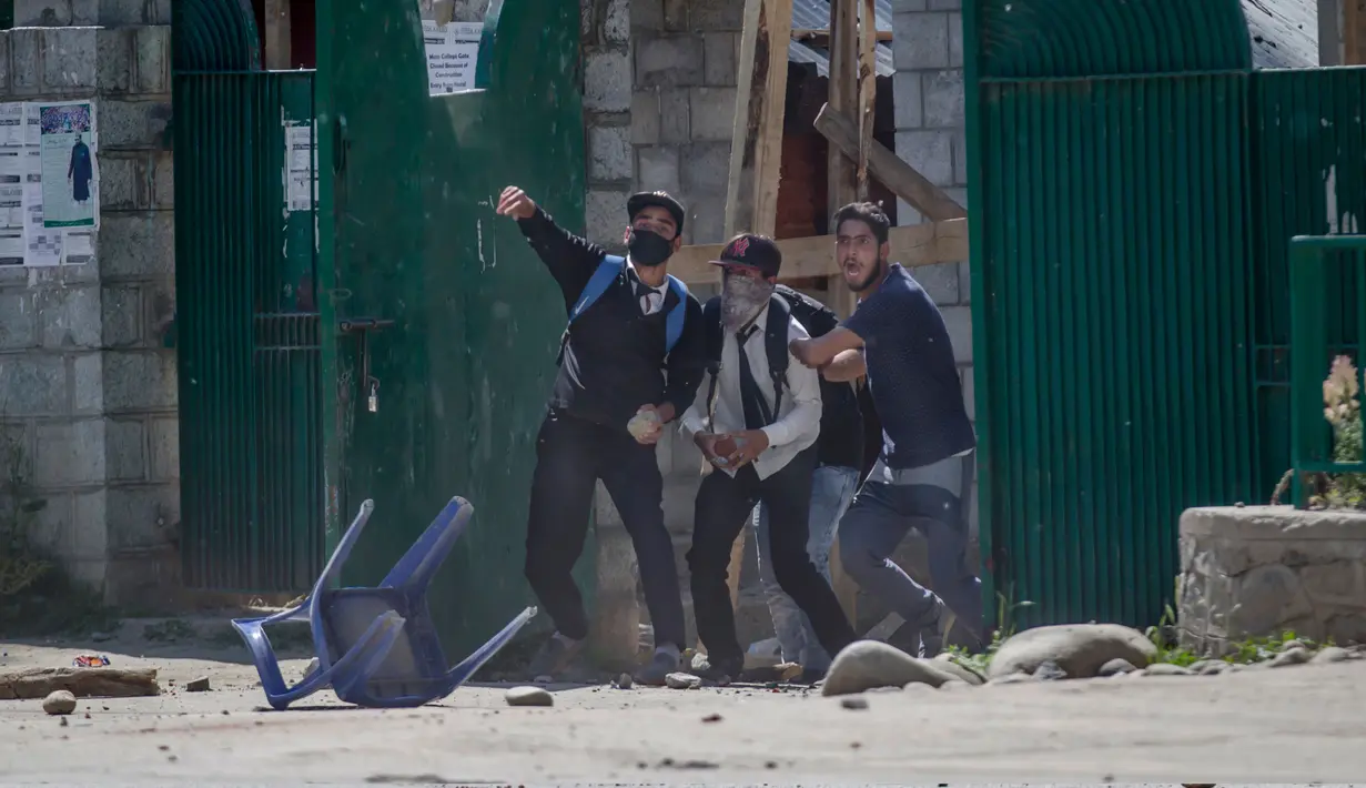 Tiga mahasiswa Kashmir melemparkan batu ke polisi India di Srinagar, Kashmir yang dikuasai India, (23/5). Bentrokan telah meningkat setelah tentara menggerebek sebuah perguruan tinggi di kota selatan Pulwama bulan lalu. (AP Photo/Dar Yasin)