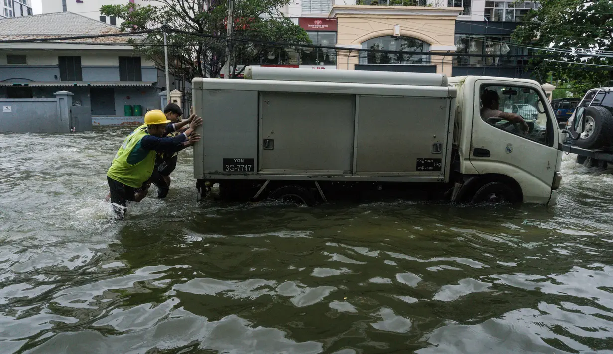 Orang-orang mendorong kendaraan yang mogok di jalan yang banjir di pinggiran Yangon, Myanmar  (17/8/2022). Hujan lebat sejak larut malam 16 Agustus menyebabkan kemacetan lalu lintas dan kesulitan bagi para komuter di kota Yangon dengan beberapa jalan masih terendam banjir.  (AFP/Stringer)