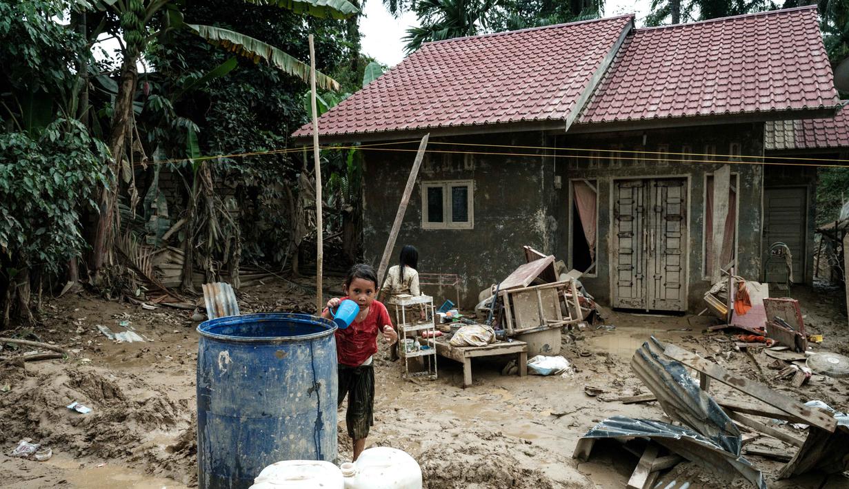 Lumpur sisa banjir, debu, serta kualitas udara yang menurun menjadi faktor utama yang dapat memperburuk kesehatan anak-anak, terutama saluran pernapasan. Tampak dalam foto, seorang anak perempuan mengambil air dari tangki penyimpanan di Babo, Aceh Tamiang, pada Senin 15 Desember 2025. (Yasuyoshi CHIBA/AFP)