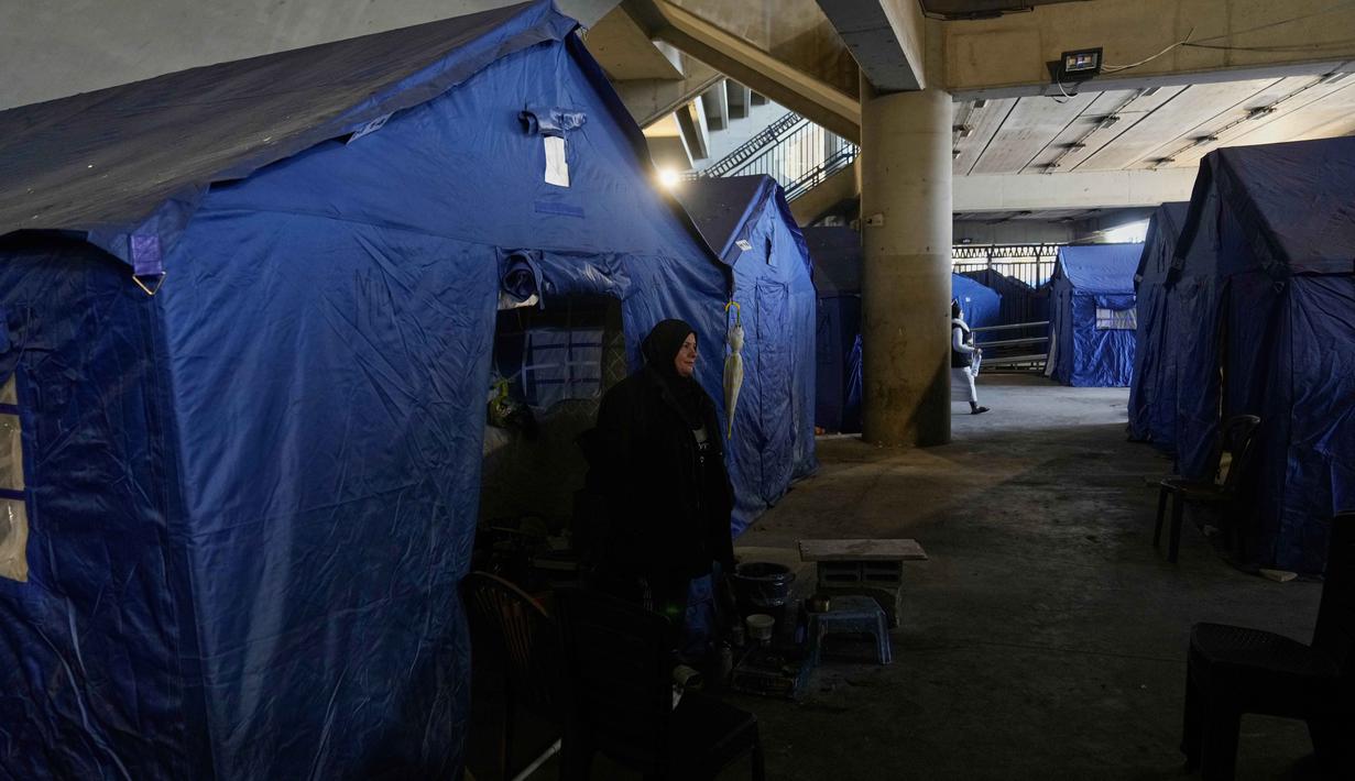 Di dalam area stadion disediakan sejumlah tenda, berikut fasilitas dasar seperti air dan listrik untuk memberikan tempat bernaung bagi keluarga yang mengungsi. Tampak dalam foto, seorang wanita pengungsi berdiri di samping tenda-tenda yang didirikan di dalam Camille Chamoun Sports City Stadium, yang telah diubah menjadi tempat penampungan bagi orang-orang yang melarikan diri dari serangan udara Israel di Lebanon selatan, Beirut, Lebanon, Rabu 8 April 2026. (AP Photo/Bilal Hussein)