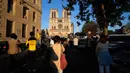 Orang-orang berhenti di depan Katedral Notre-Dame yang kembali membunyikan lonceng utamanya di Paris, Rabu (15/4/2020). Lonceng utama katedral kembali dibunyikan setelah satu tahun mengalami kebakaran yang sampai mengejutkan seluruh warga dunia. (AP/Christophe Ena)