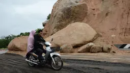 Pasangan mengendarai sepeda motor melewati batu-batu besar di jalan raya menuju bandara Narathiwat menyusul tanah longsor setelah hujan lebat di Thailand selatan (25/11/2019). Wilayah selatan Thailand akan memasuki musim hujan lebat tiga bulan dari November hingga Januari. (AFP/Madaree Tohlala)