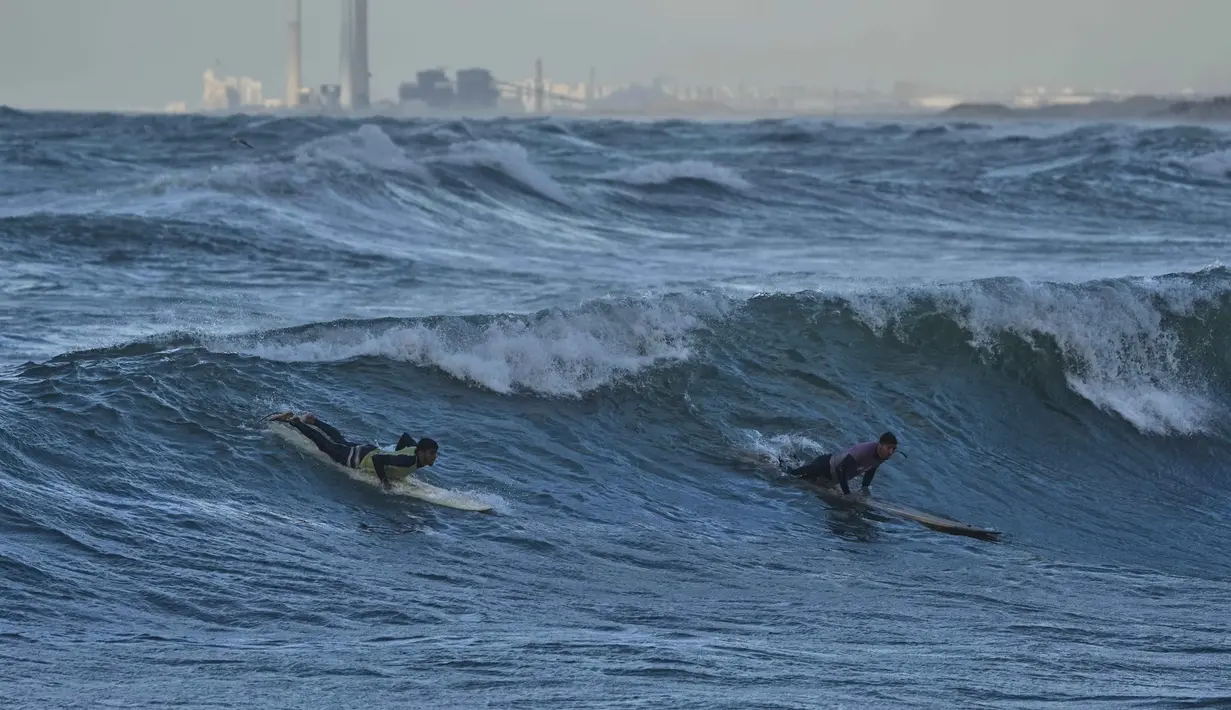 Diketahui, berselancar di Gaza merupakan hal baru, berbeda dengan pantai-pantai terkenal California, Australia, atau Afrika Selatan. Tampak dalam foto, warga Palestina, Khalil Abu Jayyab (kanan) dan Tahseen Abu Assi berselancar di pantai Kota Gaza, Minggu, 28 Desember 2025. (AP Photo/Jehad Alshrafi)