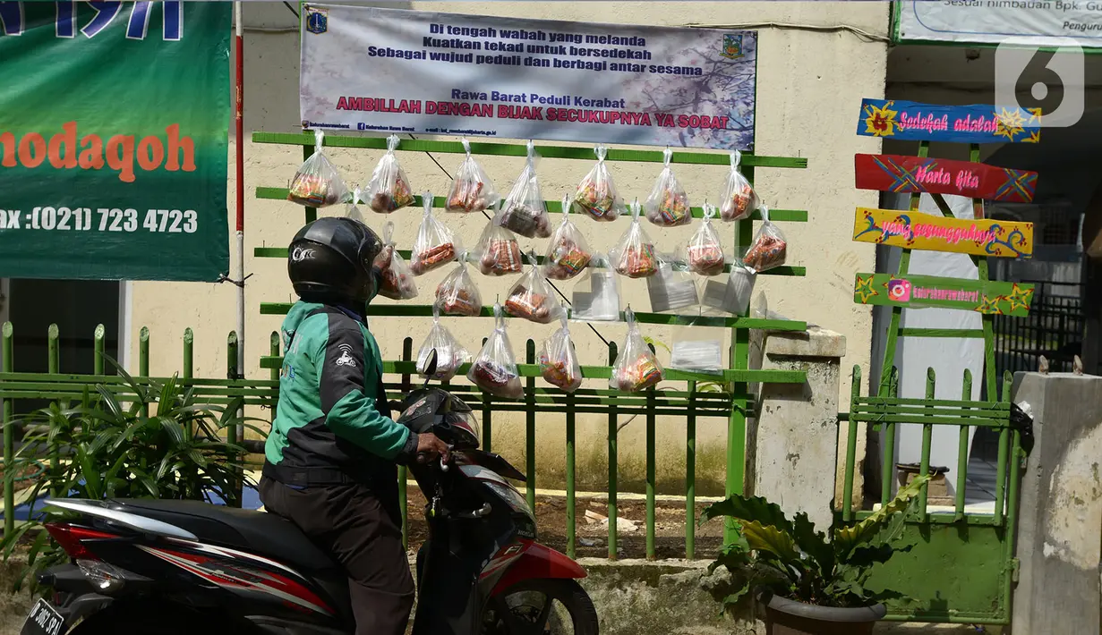 Pengemudi ojek online mengambil sembako yang digantung di rak kayu di kawasan Rawa Barat, Jakarta Selatan, Kamis (14/5/2020). Selama masa pandemi COVID-19, pihak kelurahan dan masjid sekitar menyediakan paket berisi mi instan, telur, dan masker untuk warga yang membutuhan. (merdeka.com/Imam Buhori)