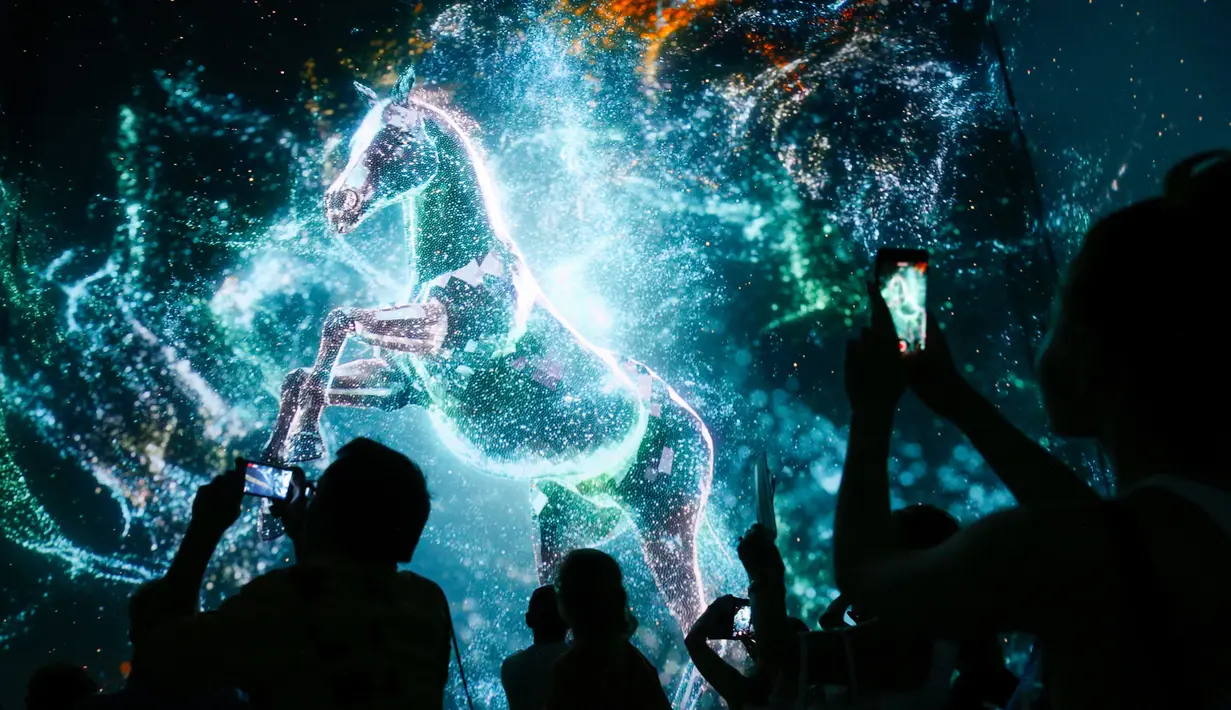 Pengunjung mengambil gambar kuda saat menyaksikan pertunjukan cahaya dalam pameran untuk mempromosikan Piala Dunia 2022 di museum multimedia Qatar Elements, Gorky Park, Moskow, Rusia, Kamis (12/7). (Maxim ZMEYEV/AFP)